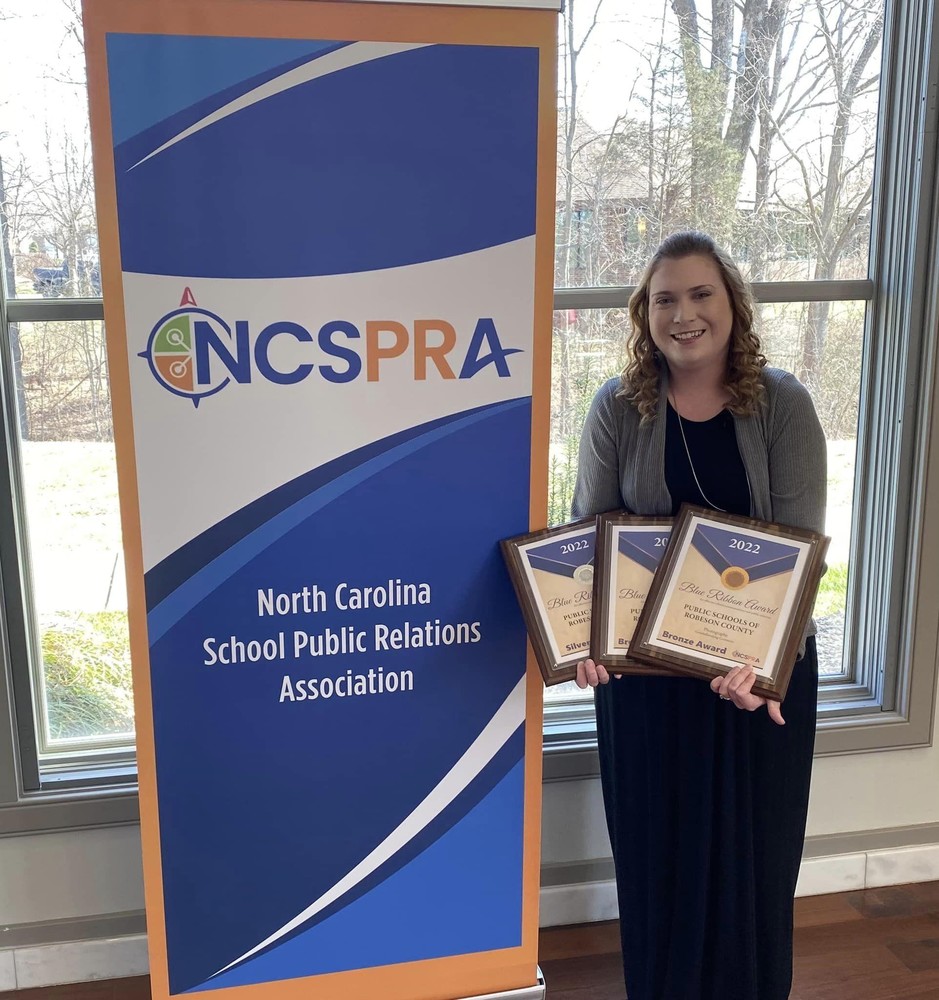 PSRC Chief Communications Officer Jessica Horne stands recently with  North Carolina School Public Relations Association  Blue Ribbon Awards for the district's communication excellence